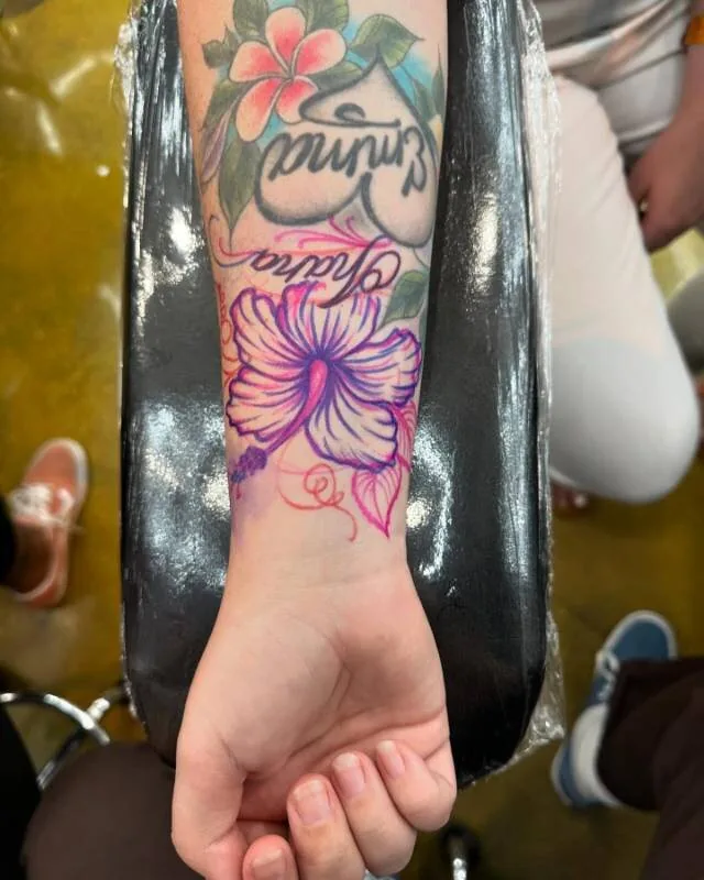 Magenta hibiscus addition by Julian (xwildxlovex) — added to a pre-existing forearm composition that already had plumeria and an ornate 'Ohana Emma' script, at Ohana Tattoo Company, Waikiki, Hawaii.